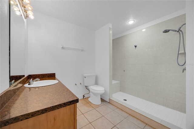 bathroom featuring toilet, a tile shower, vanity, a textured ceiling, and tile patterned flooring