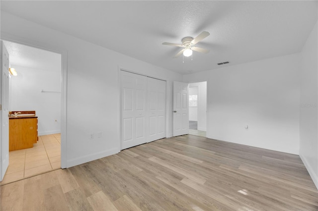 unfurnished bedroom featuring light wood-type flooring, visible vents, a textured ceiling, and ensuite bath