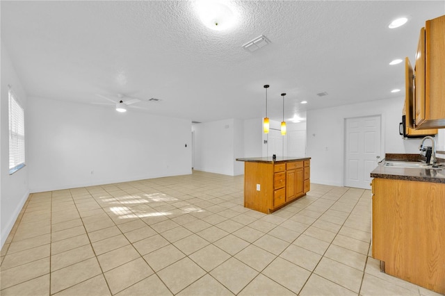 kitchen featuring light tile patterned floors, visible vents, brown cabinetry, a kitchen island, and a sink