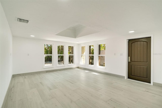 spare room featuring light wood-style flooring, recessed lighting, visible vents, baseboards, and a raised ceiling