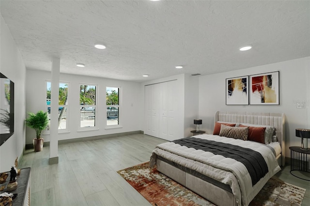 bedroom with a textured ceiling, recessed lighting, wood finished floors, baseboards, and a closet