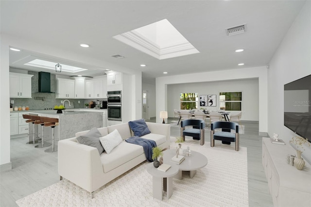 living area with a skylight, a raised ceiling, visible vents, and recessed lighting