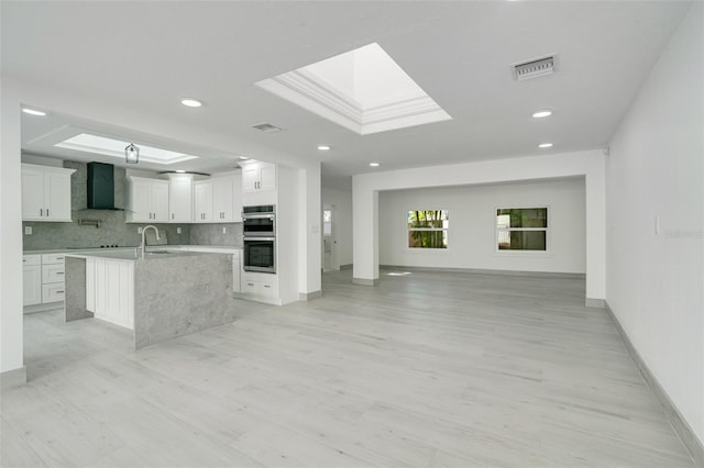 kitchen with visible vents, open floor plan, wall chimney range hood, double oven, and a sink