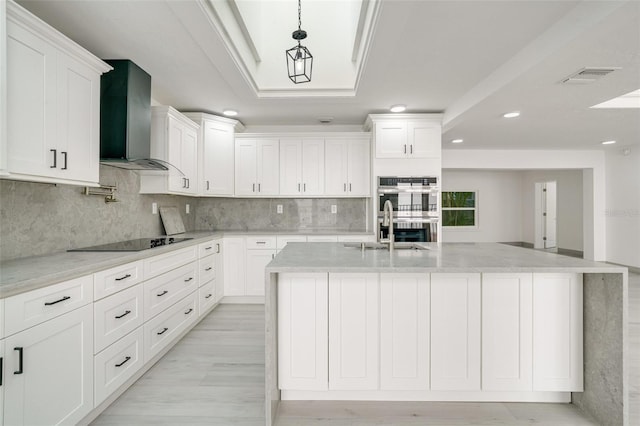 kitchen featuring white cabinets, black electric stovetop, stainless steel double oven, wall chimney range hood, and a sink