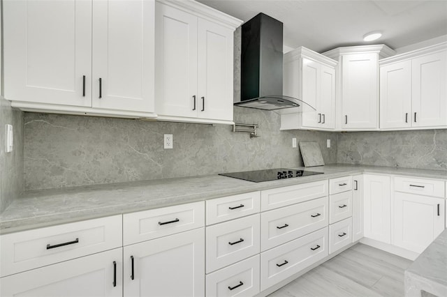 kitchen featuring light stone countertops, white cabinets, wall chimney exhaust hood, and black electric cooktop