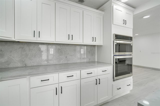 kitchen featuring double oven, white cabinetry, baseboards, light wood-style floors, and decorative backsplash