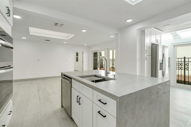 kitchen featuring a center island with sink, stainless steel appliances, visible vents, white cabinetry, and a sink