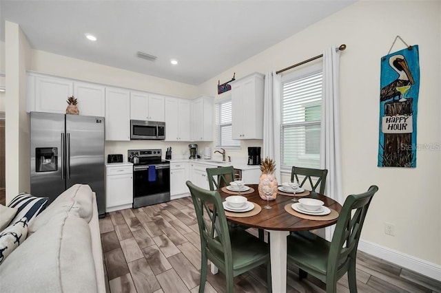 kitchen featuring visible vents, stainless steel appliances, wood finish floors, white cabinetry, and a sink