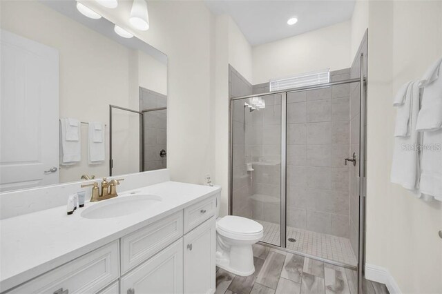 full bath with toilet, a stall shower, vanity, and wood finish floors