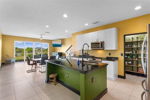 kitchen featuring stainless steel appliances, dark countertops, visible vents, white cabinetry, and an island with sink