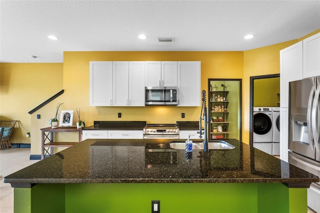 kitchen featuring light tile patterned floors, an island with sink, stainless steel appliances, white cabinetry, and separate washer and dryer