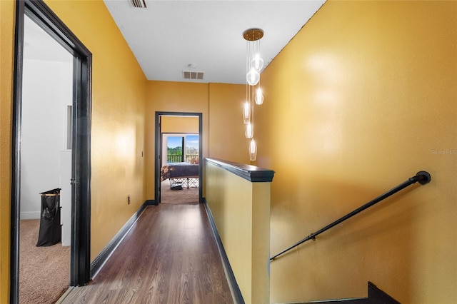 hallway with dark wood-type flooring, baseboards, visible vents, and an upstairs landing