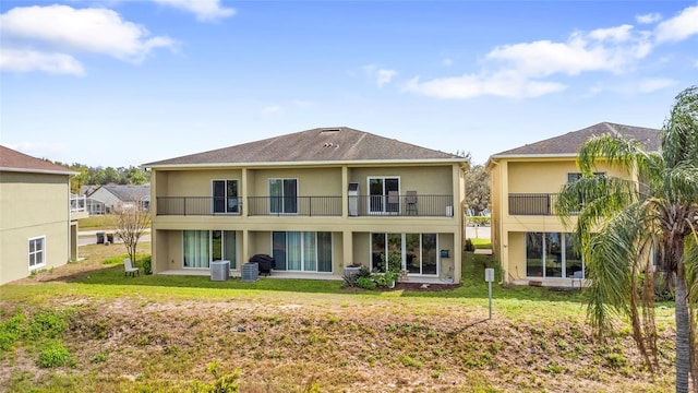 back of house featuring a lawn, a balcony, and stucco siding