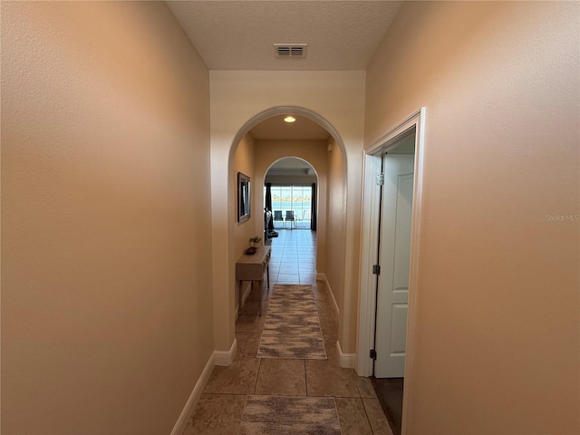 corridor with baseboards, visible vents, arched walkways, and a textured ceiling