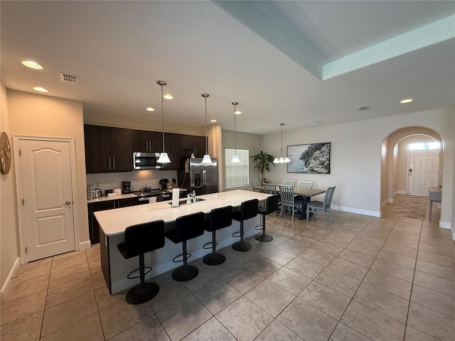 kitchen featuring visible vents, a breakfast bar, light countertops, appliances with stainless steel finishes, and arched walkways