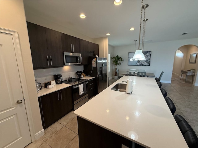 kitchen with a breakfast bar area, light countertops, appliances with stainless steel finishes, arched walkways, and a kitchen island with sink