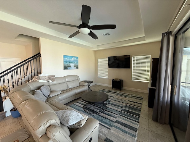 living area featuring baseboards, visible vents, a tray ceiling, ceiling fan, and tile patterned floors