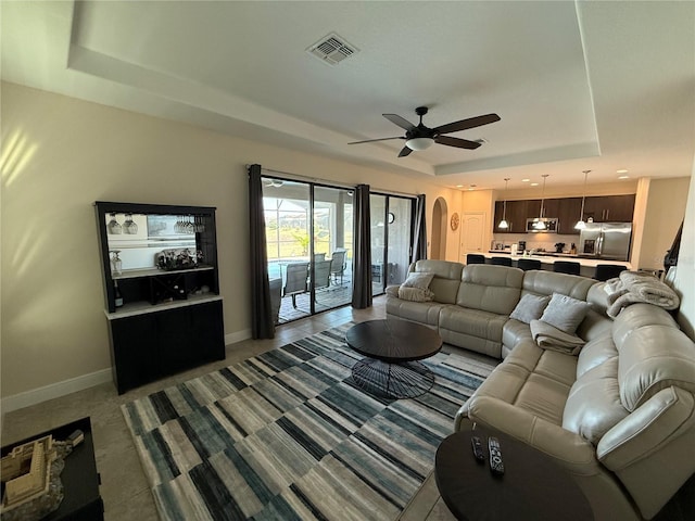 living room featuring visible vents, a ceiling fan, baseboards, arched walkways, and a raised ceiling