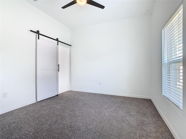 unfurnished bedroom with a barn door, baseboards, ceiling fan, and carpet flooring