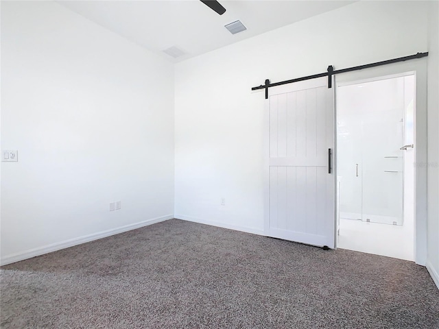 unfurnished bedroom with a barn door, visible vents, baseboards, a ceiling fan, and carpet flooring