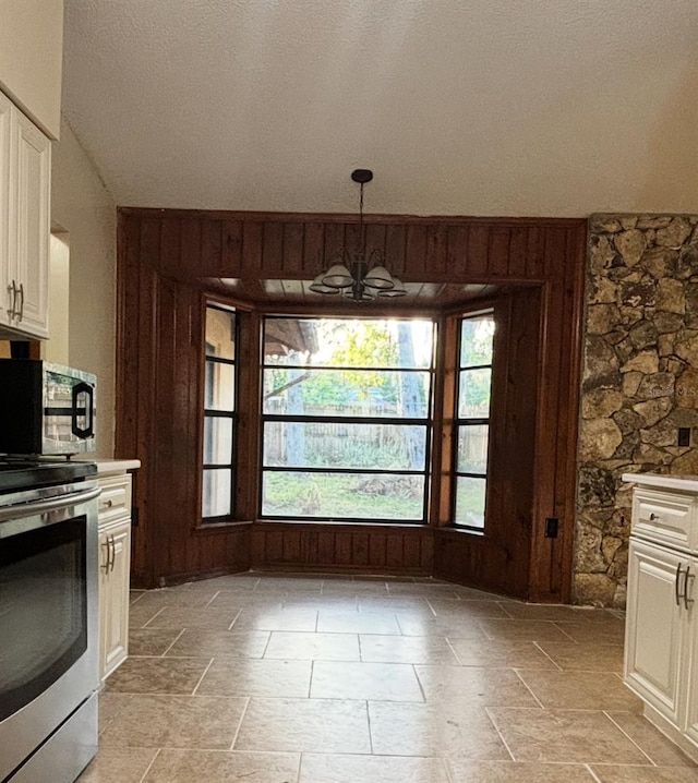 unfurnished dining area with lofted ceiling, stone finish flooring, wood walls, and an inviting chandelier