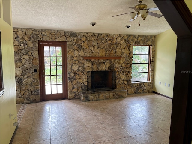 unfurnished living room featuring tile patterned flooring, ceiling fan, a textured ceiling, and a stone fireplace