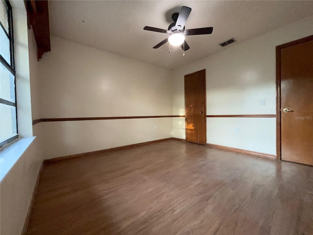 empty room with ceiling fan, a textured ceiling, wood finished floors, visible vents, and baseboards