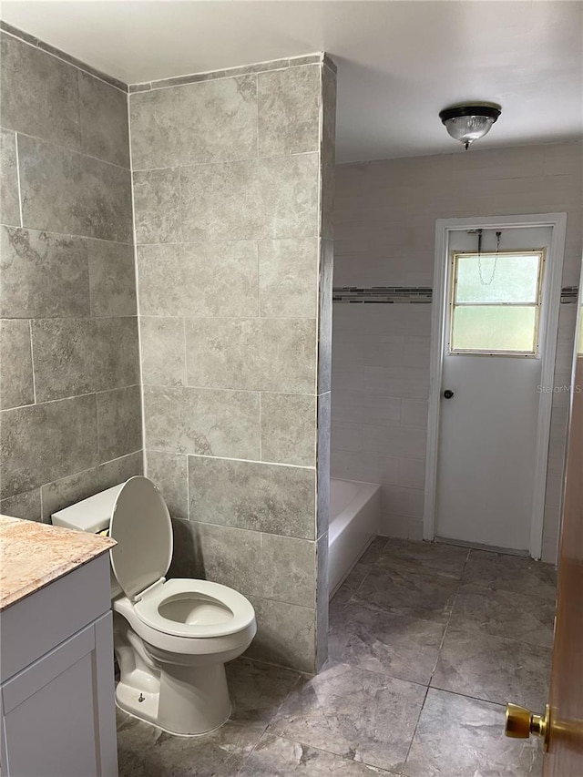 bathroom with toilet, a bathtub, tile walls, and vanity