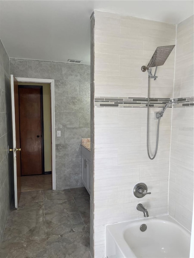 bathroom featuring washtub / shower combination, vanity, and tile walls