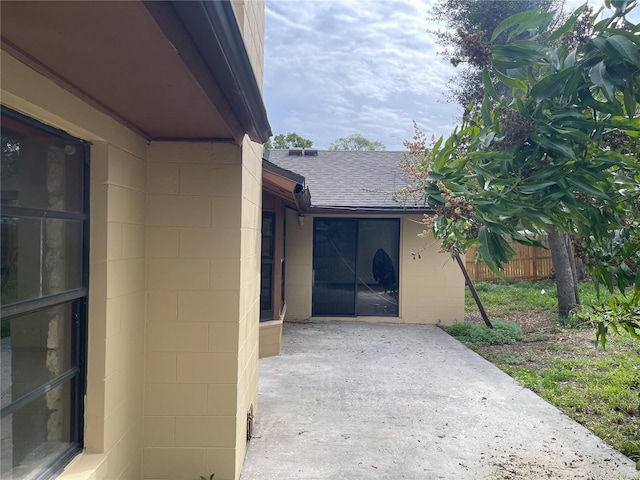 exterior space featuring roof with shingles, a patio area, concrete block siding, and fence