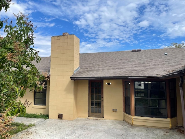 rear view of house featuring a patio, roof with shingles, a chimney, and concrete block siding