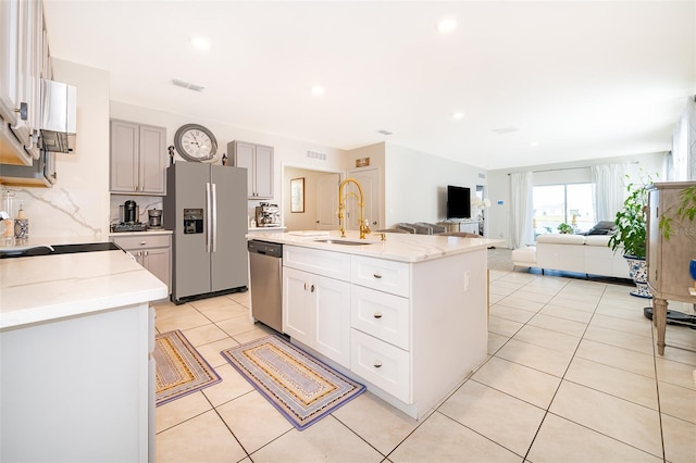 kitchen with light tile patterned floors, decorative backsplash, an island with sink, stainless steel appliances, and a sink