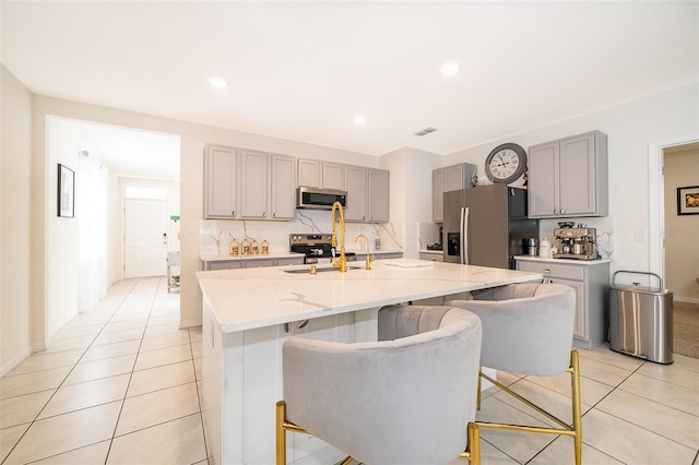 kitchen with stainless steel appliances, gray cabinets, light stone counters, and light tile patterned floors