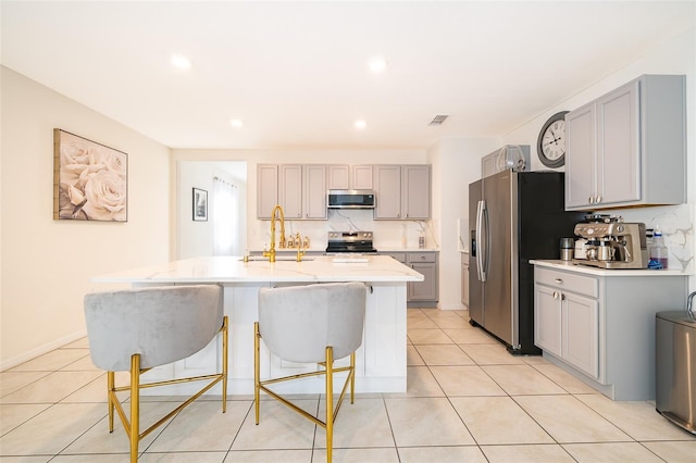 kitchen featuring a breakfast bar area, light tile patterned flooring, a sink, appliances with stainless steel finishes, and gray cabinets