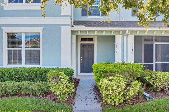 entrance to property featuring a shingled roof and stucco siding