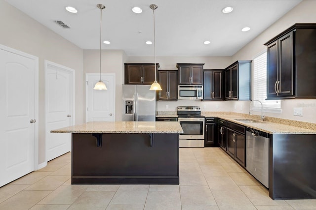 kitchen featuring light stone counters, stainless steel appliances, a sink, visible vents, and a kitchen bar