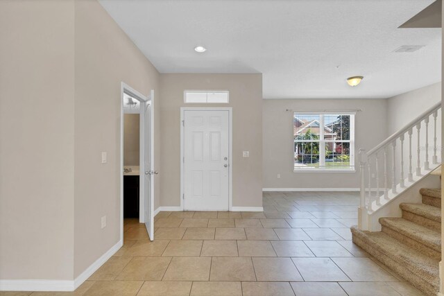 foyer entrance featuring stairs, light tile patterned floors, and baseboards