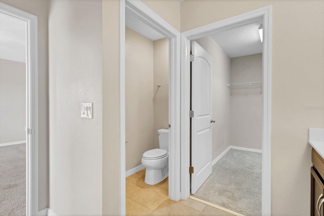 bathroom featuring a walk in closet, toilet, vanity, tile patterned flooring, and baseboards