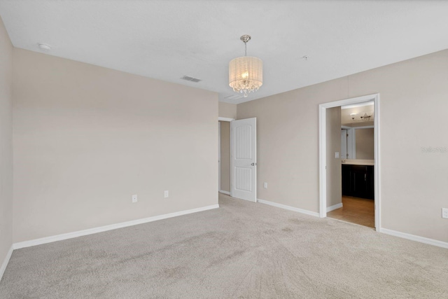 carpeted spare room with a chandelier, visible vents, and baseboards