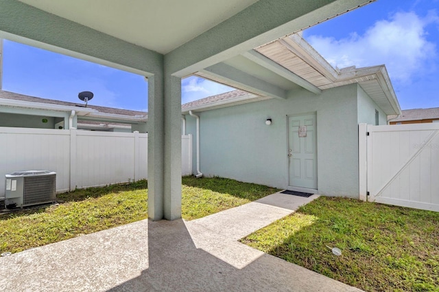 entrance to property with a yard, stucco siding, central AC unit, a gate, and fence