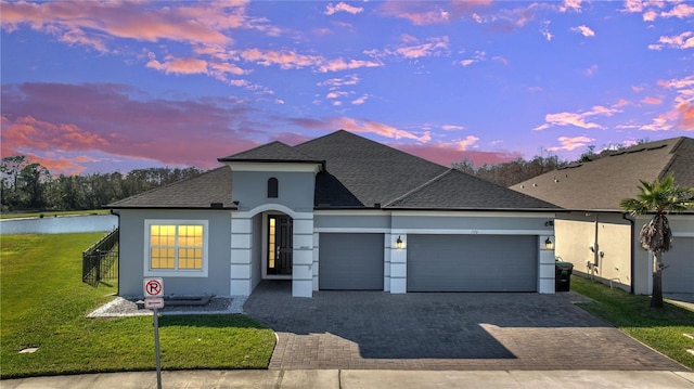 view of front facade with a garage, a lawn, roof with shingles, decorative driveway, and stucco siding