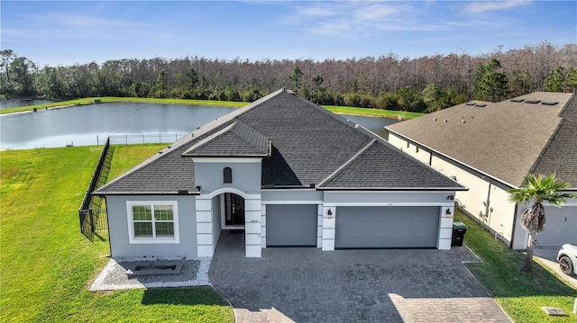 view of front of house with a garage, a shingled roof, a water view, decorative driveway, and a front lawn