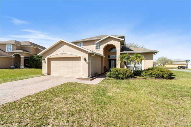 traditional-style house featuring decorative driveway, an attached garage, stucco siding, and a front yard