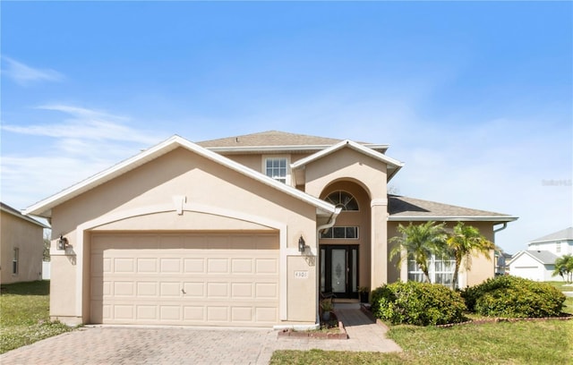 view of front of property featuring a shingled roof, decorative driveway, an attached garage, and stucco siding