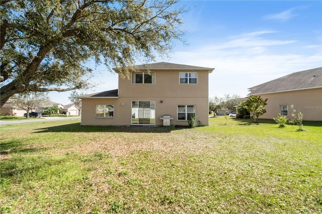 rear view of property featuring a lawn and stucco siding