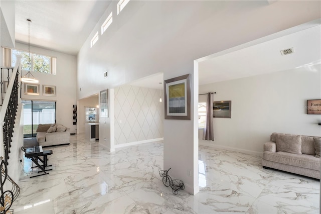 foyer entrance featuring a chandelier, an accent wall, a high ceiling, baseboards, and marble finish floor