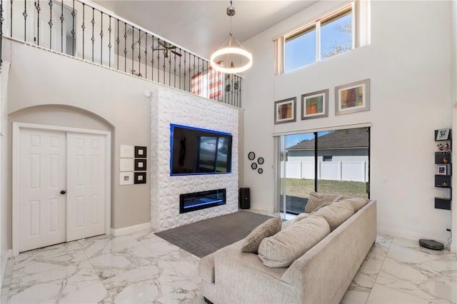 living room with marble finish floor, a high ceiling, baseboards, and a glass covered fireplace