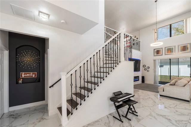 stairs with marble finish floor, a high ceiling, a fireplace, and baseboards