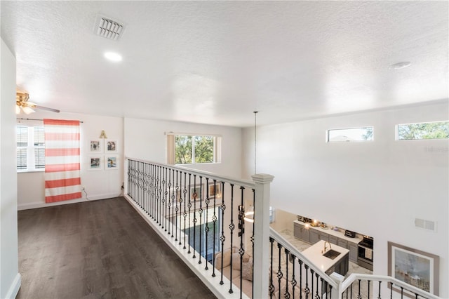 hall with visible vents, a textured ceiling, an upstairs landing, and wood finished floors