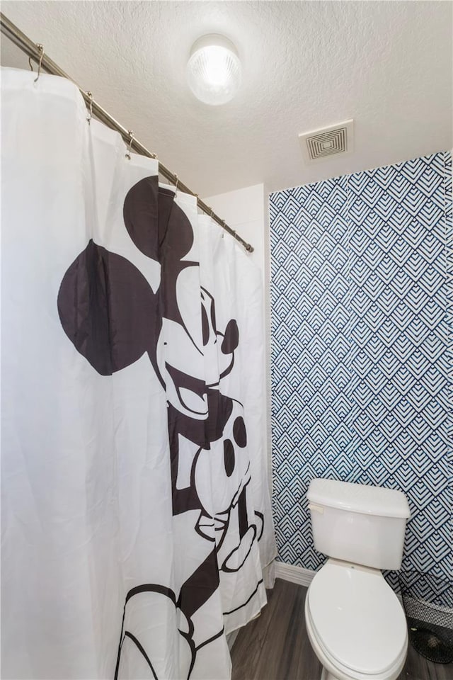 bathroom featuring visible vents, a shower with shower curtain, toilet, wood finished floors, and a textured ceiling